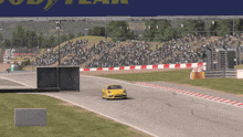 a yellow car is driving down a race track in front of a sign that says good year
