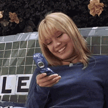 a woman is smiling while holding a blue cell phone in front of a sign that says le