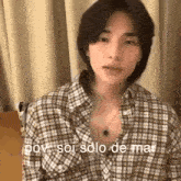 a young man wearing a plaid shirt is sitting on a bed and looking at the camera .