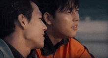 two men are looking at each other with one wearing an orange sweater