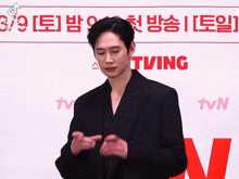 a man in a black suit stands in front of a tving sign