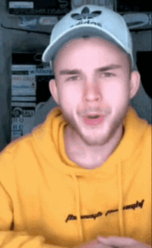 a man wearing a yellow hoodie and a white hat with adidas on it