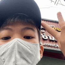 a boy wearing a mask and a hat stands in front of a sign that says ' a ' on it
