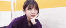 a woman in a purple shirt with her hand on her chin