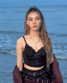 a woman in a black crop top stands in front of a body of water