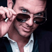 a man wearing a suit and tie is adjusting his sunglasses and smiling .
