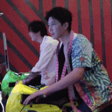 a man in a colorful shirt is riding a yellow scooter