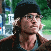 a man wearing glasses and a beanie is looking at something