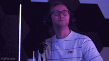 a man wearing headphones and a striped shirt is standing in front of a microphone ..