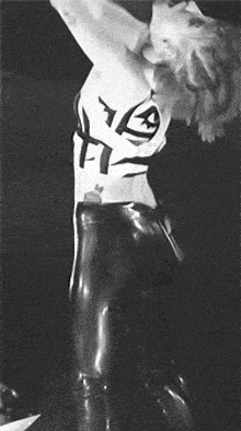 a black and white photo of a woman wearing latex pants and a white shirt with the letter a on it