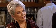 an older woman wearing a necklace and earrings is sitting at a bar