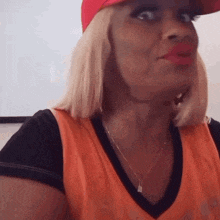a woman wearing an orange shirt and a red hat is making a face .