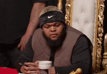 a man with a beard wearing a nike headband is sitting on a throne looking at his phone .
