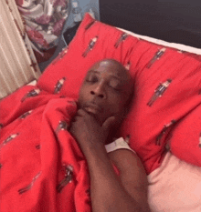 a man is laying in bed with a red blanket and a red pillow with soldiers on it