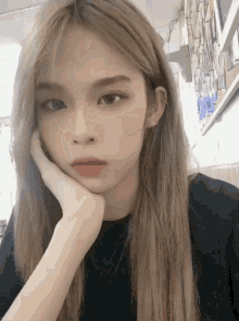 a girl with long blonde hair is taking a selfie with her hand on her face .