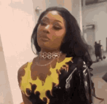a woman wearing a yellow top with flames on it and a choker is standing in a room .