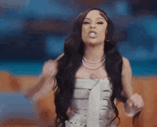 a woman with long black hair is wearing a white dress and a necklace and making a funny face .