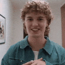 a young man with curly hair is wearing a blue shirt and a ring on his finger
