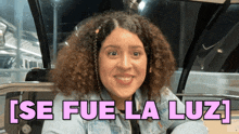a woman with curly hair is smiling in front of a sign that says ' se fue la luz '