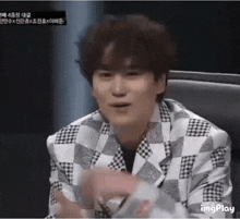 a man in a checkered jacket is sitting in a chair and clapping .