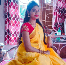 a woman wearing a yellow saree and a red blouse sits on a bed