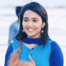 a woman wearing a blue shirt and a brown purse smiles
