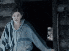 a woman in a blue and black striped hoodie is standing in a dark room