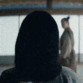 a woman with long black hair is standing in front of a window with a man in the background .