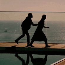 a silhouette of a man and a woman dancing on a balcony overlooking the ocean