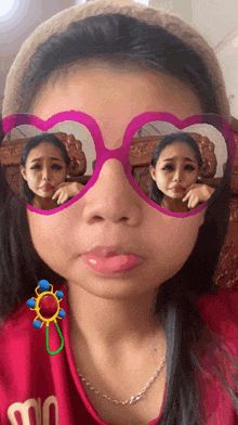 a girl wearing pink heart shaped sunglasses has a sticker on her ear that says " m "