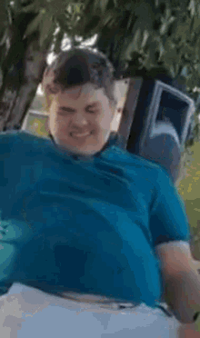 a man in a blue shirt is sitting in a chair with his arms outstretched in front of a tree .
