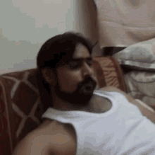 a man with a beard is laying on a couch in a white tank top