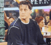 a man wearing a blue sweater is sitting in front of a sign that says perk