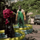 a man in a red robe is spraying a man in a green apron with a hose