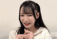 a young girl with long hair is smiling and making a heart shape with her hands .
