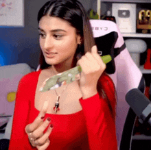 a woman in a red shirt is holding a green item in her hand .