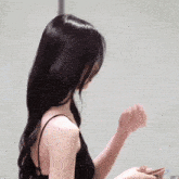 a woman with long black hair wearing a black tank top is standing in front of a white wall