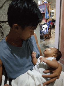 a man is holding a baby in his arms and the baby is wearing a white shirt