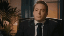 a man in a suit and tie is sitting in a chair and looking at the camera .