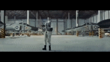 a man in a military uniform is standing in a hanger surrounded by fighter jets .