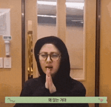 a woman wearing a black hoodie and glasses praying