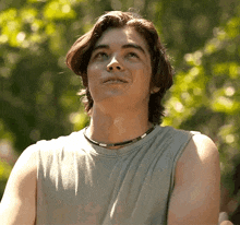 a young man wearing a gray tank top and a necklace looks up at the sky .