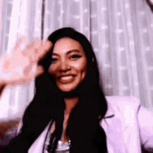 a woman with long black hair is smiling and waving at the camera .