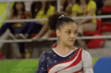 a female gymnast wearing an american flag outfit is standing in front of a crowd of spectators .