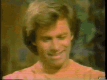a close up of a man 's face with a pink shirt on