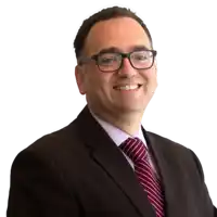 a man wearing glasses and a suit is smiling for the camera .