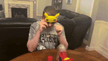 a man wearing a pikachu mask sits at a table in a living room