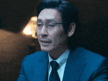 a man wearing glasses and a blue suit is sitting in a dark room