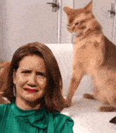 a woman in a green top is crying while a cat is standing behind her