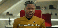 a man in a star trek uniform is sitting in a red chair and saying `` thank you , number one . ''